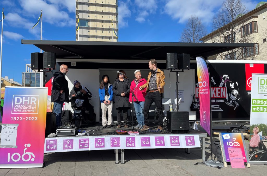 Fem av Skellefteås kommunpolitiker står på en scen intill en roll-up med texten DHR 1923 - 2023.