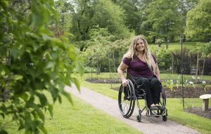 En kvinna i rullstol på en grusgång i en lummig park.