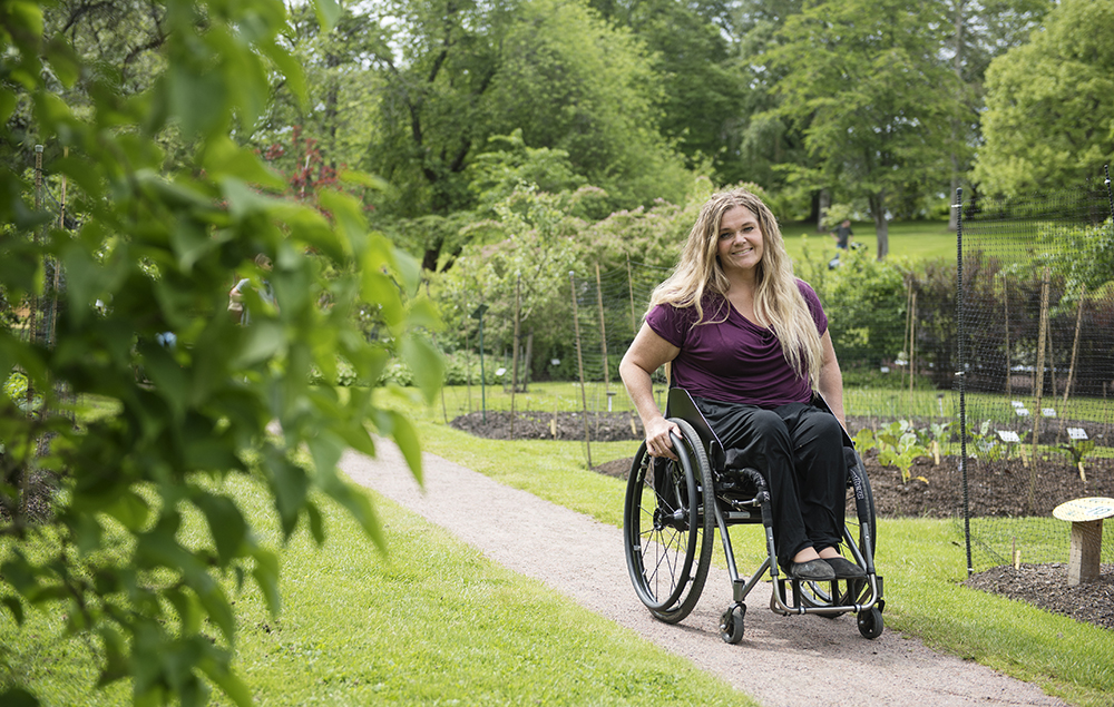 En kvinna i rullstol på en grusgång i en lummig park.