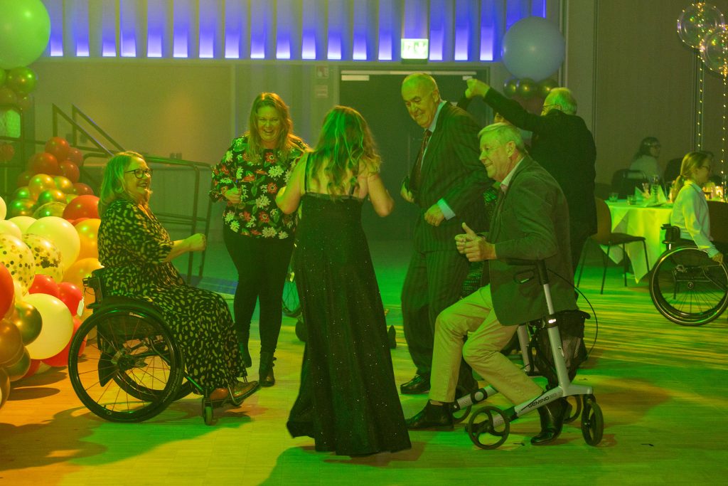 På ett dansgolv dansar flera personer med inlevelse. En av dem dansar sittande på sin rollator och en dansar sin rullstol.