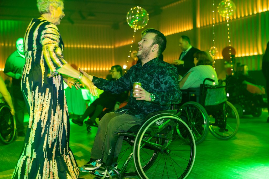 Ett festklätt danspar där kvinnan buggar stående och mannen buggar sittande i rullstol. 